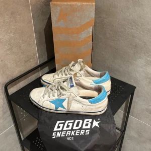 Golden Goose Superstar - Tja! Säljer dess riktigt schyssta vita/ljusblå Golden Goose superstar! Dojjorna är i bra skick, slitningarna är design! Size 39/40. Allt OG medföljer. Skriv vid funderingar!