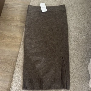 Brun stickad kjol från Vila  - Mysig brun stickad kjol från Vila med slits på sidan och bred ribbad kant nedtill. Oanvänd, storlek M. Säljer för 200kr