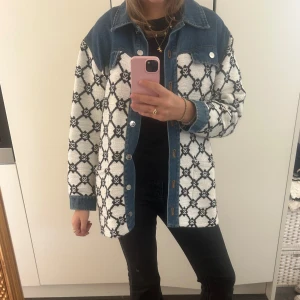 Mönstrad overshirt från Sandro - Säljer en snygg overshirt med blå denimkrage och axelparti. Jackan har vit bas med svart mönster, knappar framtill och långa ärmar. Perfekt för dig som vill ha en unik och trendig look.