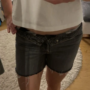 Grå jeansshorts med råa kanter - Säljer ett par grå jeansshorts med råa, fransiga benslut och klassisk femficksdesign. Shortsen har knappgylf och bälteshällor. Perfekta för en avslappnad stil och passar till det mesta.