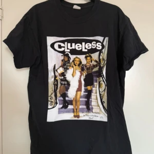 Svart Clueless t-shirt från Gildan - Svart t-shirt med stort tryck från filmen Clueless på framsidan. Klassisk passform med rund hals och korta ärmar. Tillverkad i 100% bomull, perfekt för dig som gillar filmnostalgi och streetstyle.
