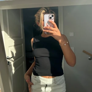 Svart croppad linnetopp - Säljer en svart croppad linnetopp med rund halsringning. Toppen är ärmlös och har en tight passform, perfekt för varma dagar eller som ett basplagg i garderoben. 