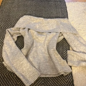 Grå stickad offshoulder-tröja från Gina Tricot - Säljer en grå stickad tröja från Gina Tricot med bred offshoulder-krage. Tröjan är mjuk och har långa ärmar, perfekt för lager-på-lager och en chill look. Passar dig som gillar enkel men snygg stil.