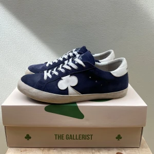Marinblå sneakers från The Gallerist - Snygga marinblå sneakers från The Gallerist med vita detaljer och en unik klöverdetalj på sidan. Skorna är i ett fin skick men har små deffekter på sulan bild 4,5 knapp synbara när man har de på sig. Nypris 2400 köpta i somras. 