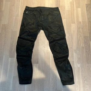 Cargobyxor i camouflage från G-Star RAW - Säljer ett par G-Star RAW Motac Deconstructed cargobyxor i camouflage. Byxorna har slim passform, förstärkta partier vid knä och vader samt flera fickor. Perfekta för dig som gillar streetwear och vill sticka ut med snygga detaljer. Storlek: 32/32