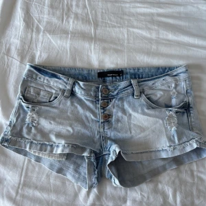 Lågmidjade jeansshorts  - Säljer ett par ljusblå jeansshorts från tally weijl med slitna detaljer, fransig kant och tre synliga knappar framtill. Shortsen har klassiska fickor både fram och bak och är perfekta för varma dagar. Liten ljusrosa fläck på ena bakfickan men inget man tänker på❤️