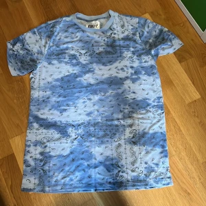 Bandana mönstrad t-shirt från Street Vibes - Säljer en blå och vit t-shirt från Street Vibes med bandanamönster över hela tröjan. T-shirten har normal passform och är kortärmad, perfekt för en avslappnad stil.