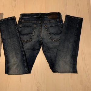 Slim fit jeans Glenn - Mörkblå slim fit jeansmodell Glenn med klassisk femficksdesign och snygga slitningar. Byxorna har normal midja och raka ben, perfekta för en clean och stilren look.