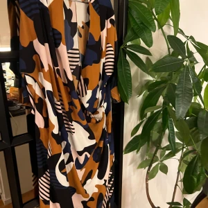 Mönstrad omlottklänning från Monki - Säljer en färgstark omlottklänning från Monki med abstrakt mönster i svart, brun, blå, rosa och vit. Klänningen har djup v-ringning och ett flowigt fall. Perfekt för dig som gillar statement-plagg och unika prints.