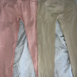 Två leggings från PrettyLittleThing - Säljer två par ribbade leggings från PrettyLittleThing Båda har hög midja och är stretchiga med mjukt material. Båda är i storlek M men de råsa är mindre  än de Beiga fast de är inte någon större skillnad 