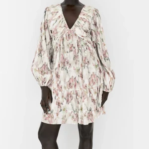 Blommig plisserad klänning med v-ringning - Superfin kortklänning med plisserat tyg och blommigt mönster i rosa och grönt på vit botten. Djup v-ringning och långa, puffiga ärmar med resår vid handlederna. Perfekt för vår och sommar!