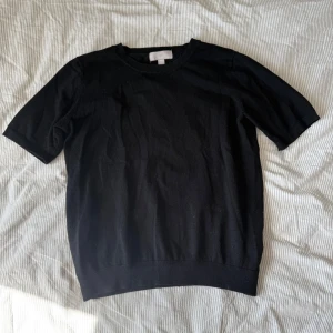 Svart kortärmad tröja från H&M - En enkel svart kortärmad tröja från H&M. Tröjan har rund halsringning och är tillverkad i ett mjukt material som passar perfekt till vardags. Klassisk och stilren design som är lätt att matcha med olika outfits.