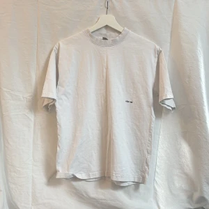 Vit t-shirt med tryck från YÔKF 989 - Vit t-shirt med enkel design och liten svart text 'YÔKF 989' på bröstet. Klassisk passform med rund hals och korta ärmar. Perfekt för en clean och stilren look.