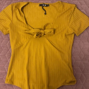 Gul ribbad body med knyt fram - Säljer en gul ribbad body från Bik Bok med korta ärmar och snygg knyt-detalj framtill. Perfekt för att piffa upp outfiten med en färgklick och en trendig touch. Använd bara en gång och i storlek S