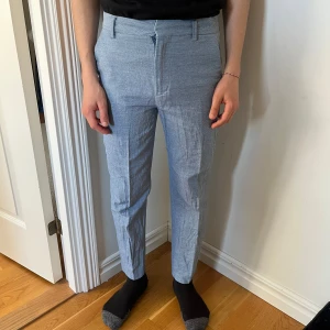 Ljusblå kostymbyxor med diskret mönster - Snygga ljusblå kostymbyxor med diskret mönster och klassisk passform. Byxorna har hällor för bälte, dragkedja och knäppning fram samt fickor både fram och bak. Perfekta för en stilren look.