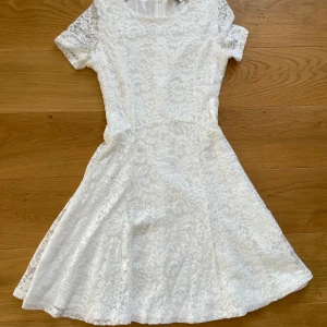 Vit spetsklänning med kort ärm - Säljer en söt vit klänning i spets med rund halsringning och korta ärmar. Klänningen har en lätt utställd kjol och dragkedja i ryggen. Storlek 158/164