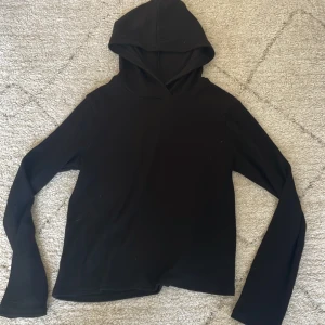 Svart hoodie från Kappahl - En enkel svart hoodie från Kappahl i storlek 158/164. Tröjan har långa ärmar och huva, perfekt för en avslappnad stil. Mjuk och bekväm, passar till många tillfällen.