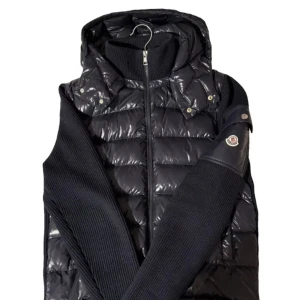 Moncler hooded cardigan  - Snygg svart dunväst från Moncler med glansig yta och huva. Västen har dragkedja framtill, ribbade stickade partier på sidorna och Moncler-logga på axeln. Perfekt för lager-på-lager och stilren look. Kan ta mer bilder på allt om de skulle behövas dock drag kedjan måste fixas för när man drar upp så blir det öppet igen och två flews  små flaws 