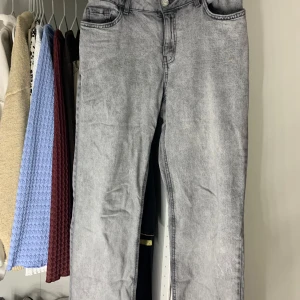 Grå jeansbyxor från Lindex - Grå jeansbyxor från Lindex i klassisk femficksmodell. Byxorna har en rak passform och är tillverkade i denim med lätt tvättad look. Knapp och dragkedja framtill samt råa kanter nertill på benen för en trendig touch.