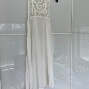 Hollister, vit  ärmlös långklänning med spetsdetaljer - Vit långklänning med ärmlös design och dekorativa spetsdetaljer upptill från Hollister.  Klänningen har en luftig och rak passform, perfekt för varma dagar eller speciella tillfällen.