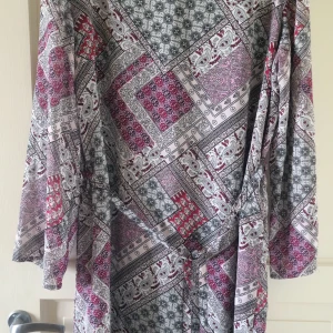 Mönstrad långärmad klänning från Giacomo - Säljer en långärmad klänning från Giacomo med ett unikt patchwork-inspirerat mönster i rött, svart, grått och vitt. Klänningen har en lös passform och är perfekt för dig som gillar färg och mönster.