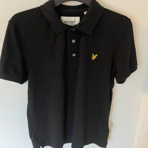 Svart Lyle & Scott piké - Klassisk svart pikétröja från Lyle & Scott. Tröjan har krage och tre knappar. Den är knappt använd och i ett mycket bra skick utan defekter. Hör av er vid funderingar
