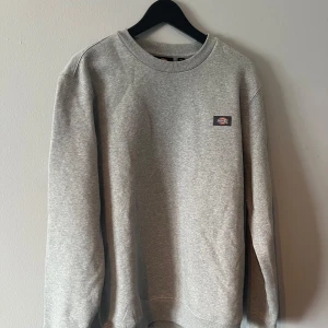 Grå sweatshirt från Dickies - Säljer en stilren grå sweatshirt från Dickies. Tröjan har en klassisk rund halsringning och en liten logotyp på bröstet. Perfekt för en avslappnad look.