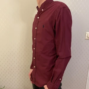 Polo Ralph Lauren skjorta  - Snygg vinröd skjorta från Ralph Lauren i slim fit. Skjortan har långa ärmar och knappar framtill. Perfekt för en stilren look. Nypris på denna är 1999kr 