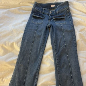 Blå bootcut jeans - Snygga blå bootcut jeans med hög midja och dubbla knappar. De har framträdande sömmar och praktiska fickor fram. Perfekta för en avslappnad stil.