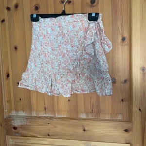 Blommig kjol från KappAhl - Söt blommig kjol från KappAhl i ljusa färger med volangdetaljer. Perfekt för varma dagar med sitt luftiga material och fina mönster. Kjolen har en omlott-look och en bekväm passform.