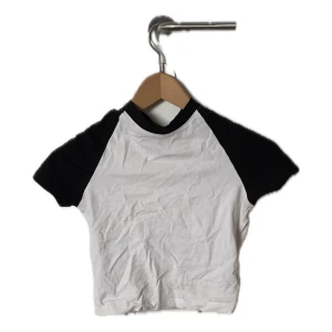 Vit och svart kortärmad t-shirt - Säljer en stilren vit och svart t-shirt med korta ärmar. Perfekt för en avslappnad look. T-shirten har en klassisk design med kontrasterande svarta ärmar och krage. Storlek S men liten i storleken.