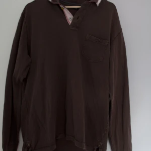 Brun långärmad pikétröja från Napapijri - Säljer en brun långärmad pikétröja från Napapijri med en liten bröstficka och en broderad norsk flagga på ärmen. 