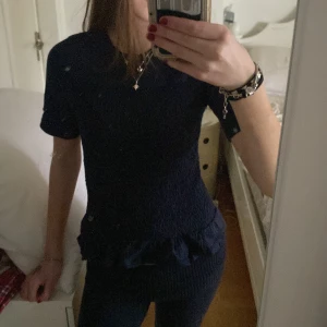 Mörkblå topp från Gina Tricot - Säljer en mörkblå topp från Gina Tricot med korta ärmar och smockdetaljer över bröstet. Toppen har en volangkant nedtill som ger en söt touch. Perfekt för en stilren look. Har använts en gång. Säljer pga att dne it används så mycket. Skriv för mer information och bilder.💕