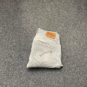 Dondup jeans - Snygga grå jeans med en klassisk femficksdesign och en läderdetalj på baksidan. De har kontrasterande sömmar och en diskret broderad detalj på bakfickan. Perfekta för en avslappnad stil.