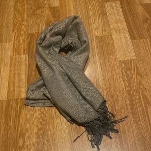 Grå kashmirhalsduk från Pashmina - Elegant grå halsduk i 100% kashmir från Pashmina. Den har ett subtilt mönster och fransar i ändarna som ger en stilren look. Perfekt för att hålla dig varm och snygg under kyliga dagar. defekt se sista bilden men inget som syns❤️