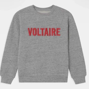 Grå Zadig tröja med röd text - Säljer en stilren grå sweatshirt med röd text 'VOLTAIRE' på bröstet. Tröjan har en klassisk rund hals och långa ärmar. Perfekt för en avslappnad look. Vill bli av med den så kom med prisförslag 