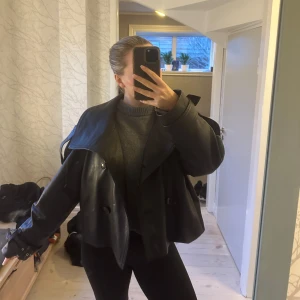 short Leather trenchcoat - Snygg kort svart skinn trenchcoat med dubbelknäppning och hög krage. Jackan har en croppad passform och justerbara spännen vid ärmsluten. Perfekt för en edgy look! Knappt använd. Ifrån hm premium 