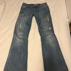 Blå bootcut jeans - Snygga blå bootcut jeans med slitna detaljer. Perfekta för en avslappnad stil. Klassisk femficksdesign och knappgylf.