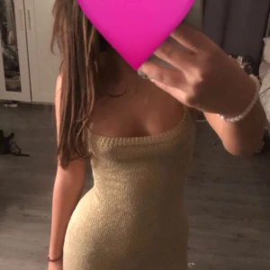 Glittrig guldfärgad klänning - Snygg glittrig guldfärgad klänning med smala axelband och snörning i ryggen. Aldrig kommit till användning! Helt ny och köpt i Spanien 