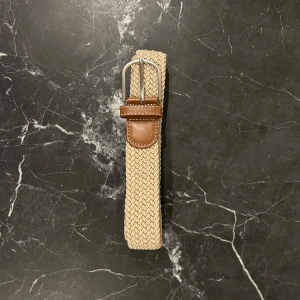 Beige flätat bälte med bruna detaljer - Snyggt beige flätat bälte med bruna skinn-detaljer och silverfärgat spänne. Perfekt för att ge en stilren touch till din outfit. 