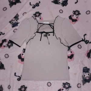 Rosa topp med volangdetaljer - Söt muted Rosa  topp från Pium med volangdetaljer och svart knytband vid halsen. Toppen har korta ärmar och ett diskret rutmönster. Perfekt för jirai kei och feminin stil.