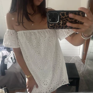 Vit axelbandslös klänning - Söt vit axelbandslös klänning med broderade detaljer och kort längd. Perfekt för sommarens varma dagar. Klänningen har en luftig passform och charmiga volanger vid ärmarna.