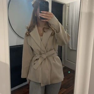 Beige knyt kappa - Säljer en jättefin beige kappa som man kan knyta runt midjan. Jackan har en klassisk design med långa ärmar och krage💗