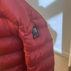 Röd dunjacka från Parajumpers - Säljer en snygg röd dunjacka från Parajumpers, modell Sheen. Jackan har en quiltad design och en praktisk huva. Perfekt för kyliga dagar med sin varma och bekväma passform.