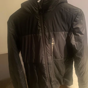 Tunn Svart jacka från Sail Racing - Säljer en stilren svart jacka från Sail Racing. Jackan har en dragkedja framtill och är perfekt för kyligare dagar. Jackan har en liten skada framtill som finns att se på bild 3 och 4. Skulle klassa jackan som en vårjacka. P.g.a skadan kan jag ta emot bud som är lägre än ursprungspriset. Inköpt på Jonells för ca 3000 kronor. Är inte 100% säker på storleken eftersom den inte har används på flera år. Gissar på att den passar 1.70-1.80 med normal kroppsbyggnad 