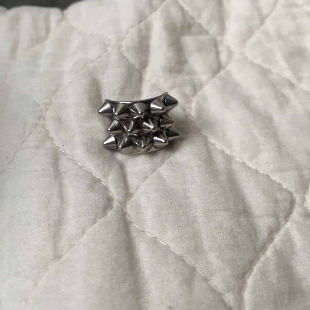 Cool ring i silverfärg med flera spetsiga nitar som ger en edgy look. Ringen har en slät insida för bekväm passform.. Asusteet.
