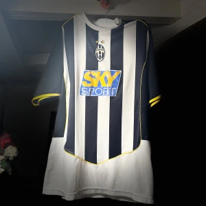 Juventus tröja med Zlatan Ibrahimovic 04/05 - Säljer en klassisk svartvit randig fotbollströja från Nike med korta ärmar och gula detaljer. Tröjan har ett stort tryck med 'SKY SPORT' på framsidan och 'BRAHIMOVIĆ 9' på baksidan. Perfekt för fotbollsfans!