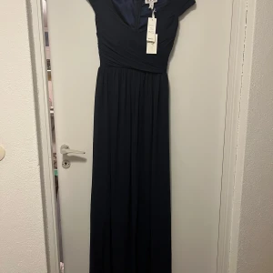 Mörkblå långklänning från NLY Eve - Elegant mörkblå långklänning från NLY Eve med v-ringning och kortärmad design. Klänningen har en smickrande omlott-look upptill och en dragkedja i ryggen. Perfekt för speciella tillfällen.