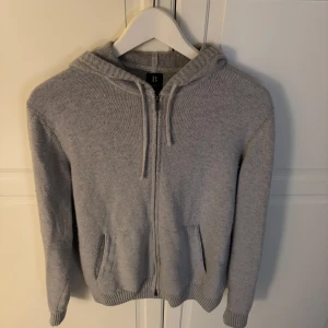 Grå Kashmir blend hoodie med dragkedja - Säljer en stilren grå hoodie med dragkedja framtill. Tröjan har en praktisk huva och två fickor. Perfekt för en avslappnad look. Storlek S