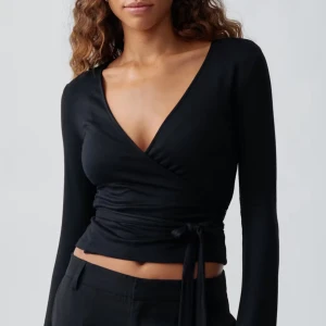 Svart omlottopp - Snygg svart omlottopp med lång ärm och knytning i midjan. Perfekt för en stilren look. Använd få antalt gånger och har inga defekter.